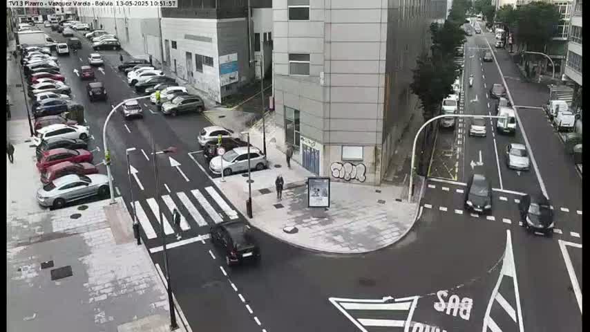 A street intersection with parked cars and several cars driving on a cloudy day.