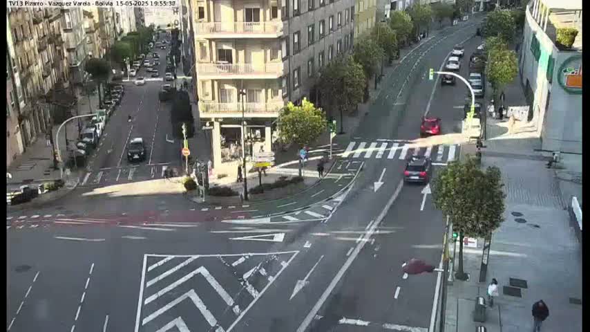 A sunny city intersection with several cars and pedestrians, featuring bike lanes and crosswalks.