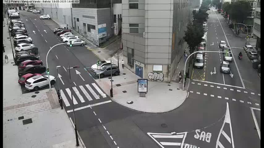 A street intersection with parked cars along the sides and several cars driving on the road, on a partly sunny day.