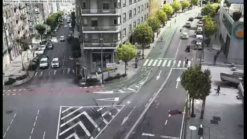 A city intersection with several cars and pedestrians on a sunny day.