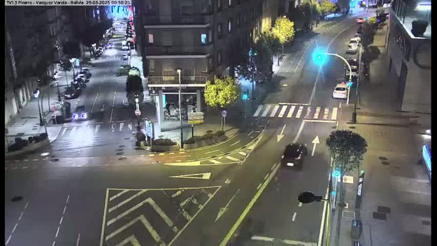 A wet, nighttime street intersection with several cars and buildings visible.