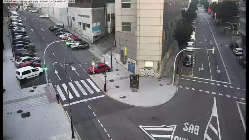 A street intersection with parked cars along the side of a building, a crosswalk, and several cars driving on a road.