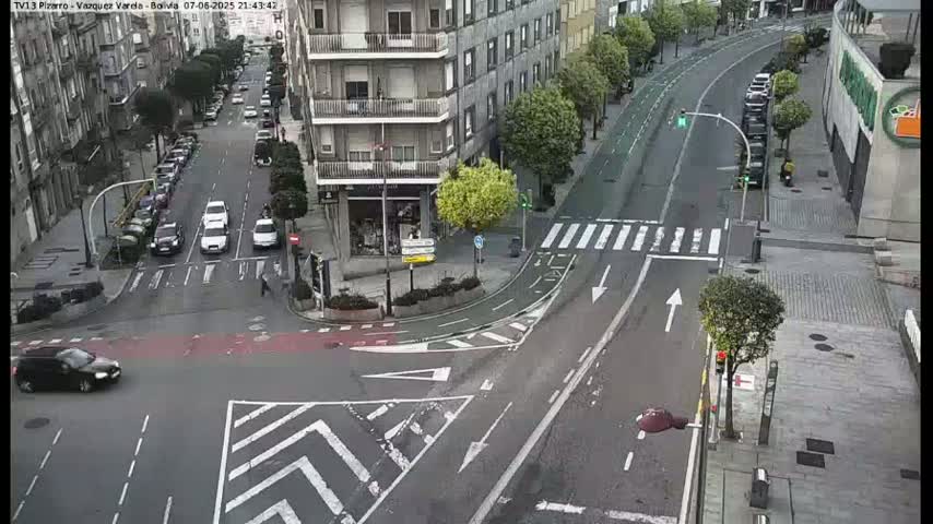 A high-angle view of a city street intersection with several cars and pedestrians, under overcast conditions.