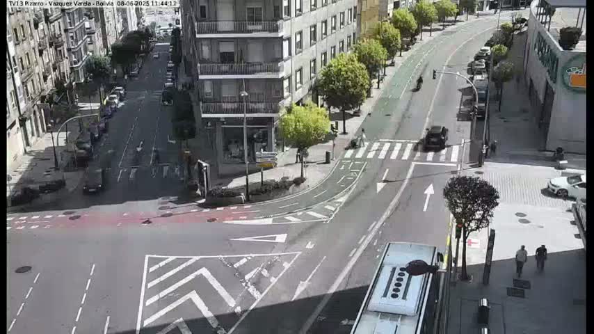 A city intersection with several cars and a bus, under a bright, sunny sky.
