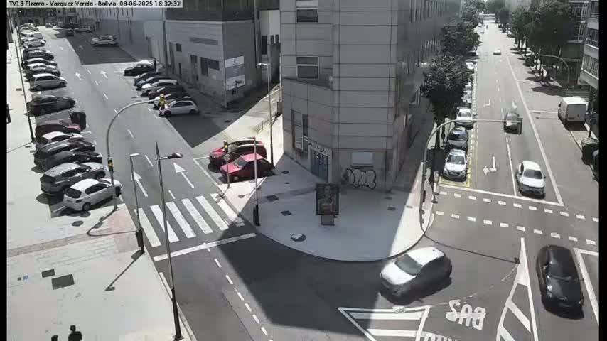 A sunny street intersection shows numerous parked and moving cars, with a building in the background.