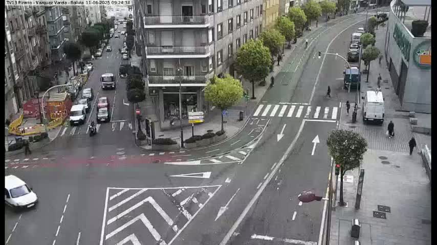 A city street intersection with light traffic and pedestrians, under an overcast sky.