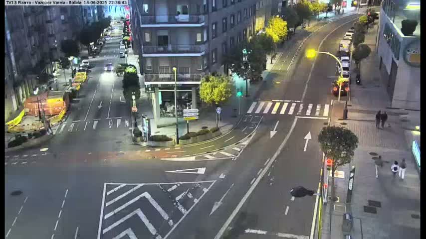 A sunny, high-angle view shows a city street intersection with several cars, buildings, and pedestrian crosswalks.