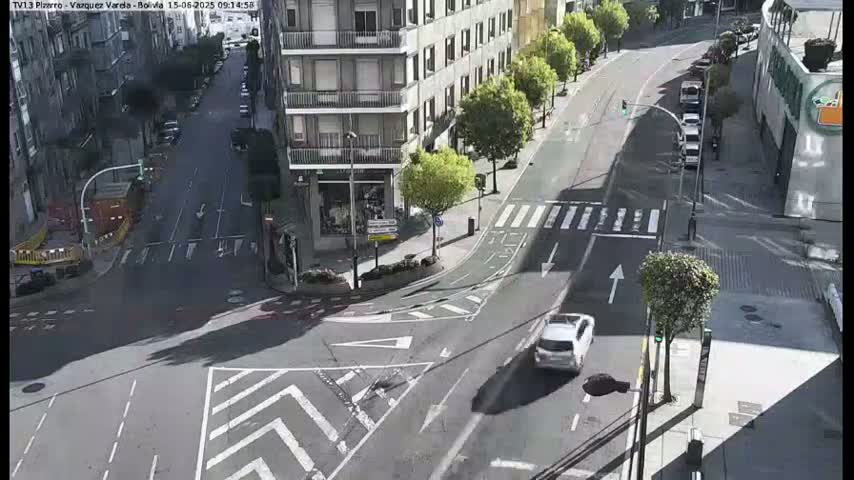 A sunny day shows a street intersection with several cars, buildings, and pedestrian crossings.