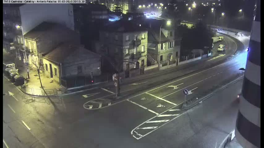 A nighttime aerial view shows a street intersection with buildings and a few vehicles, under mostly clear skies.