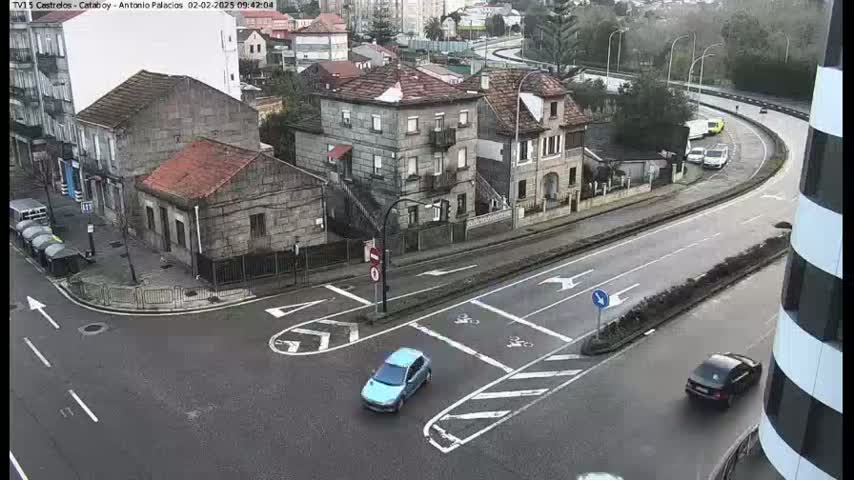 A high-angle view of a city intersection on a cloudy day, showing several buildings, cars, and road markings.