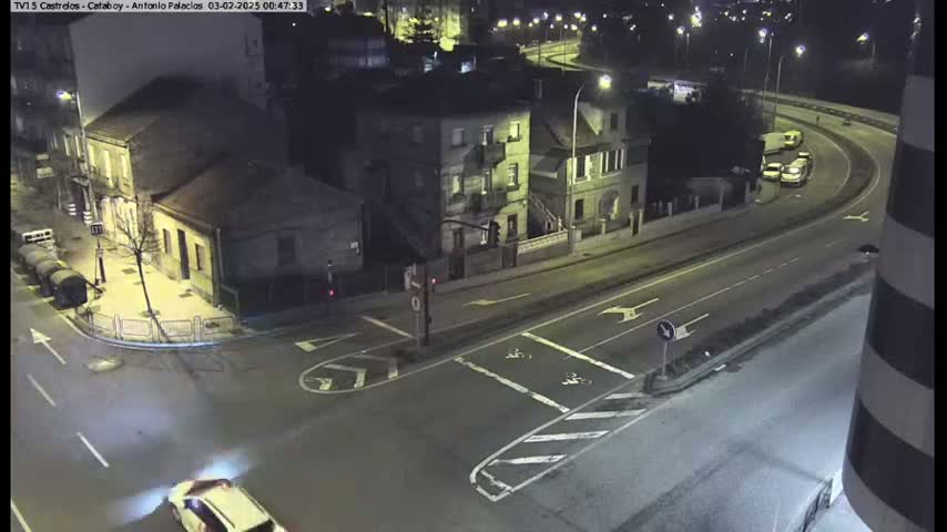 A high-angle nighttime view of a street intersection and a curving road, with several buildings and a few vehicles visible.
