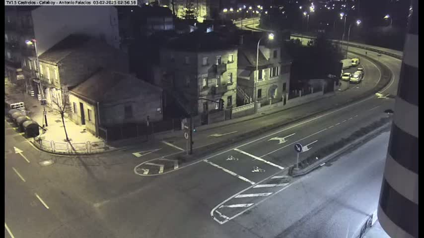 A nighttime, high-angle view of a street intersection and a curving roadway with several vehicles, bordered by buildings.