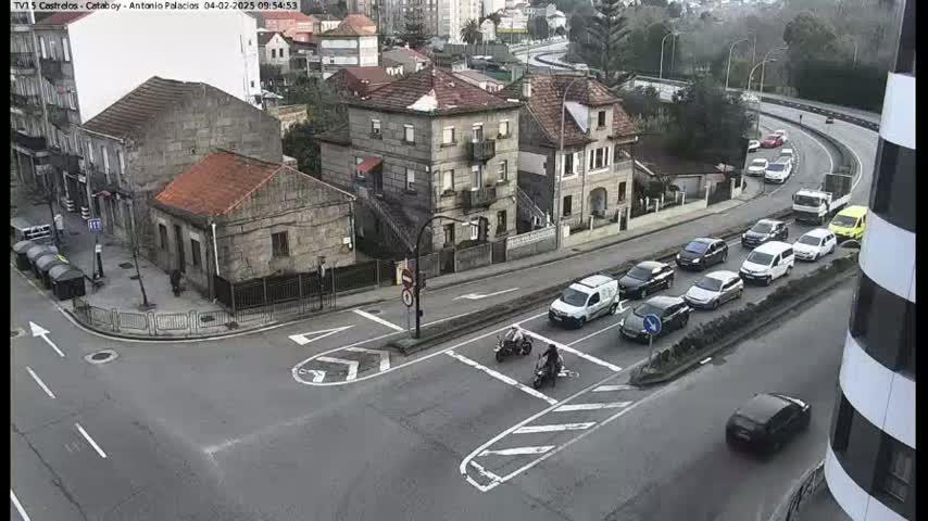 A high-angle view of a city intersection with several cars and two motorcycles, on an overcast day.
