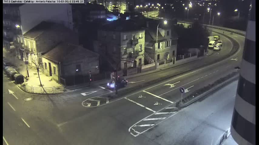 At night, a high-angle view shows a street intersection with several buildings, a few cars, and a curved road in the background.