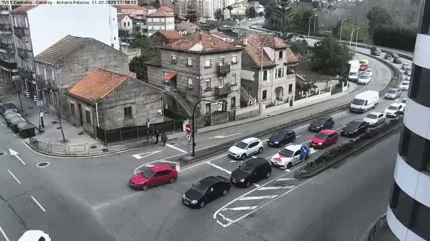 A street intersection in a town with several cars, some parked and some driving, under an overcast sky.
