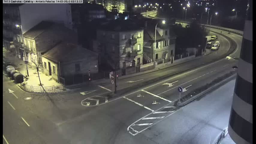 A nighttime, high-angle view shows a street intersection with several buildings and a few vehicles on a curved roadway.