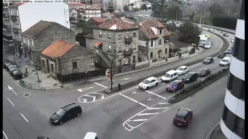 A street intersection with several cars and buildings, on an overcast day.