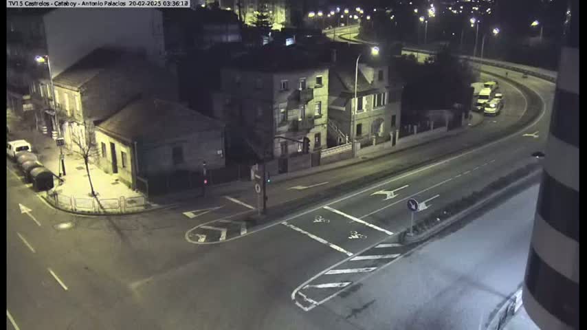 A nighttime overhead view of a street intersection with several buildings and a few vehicles, under artificial light.