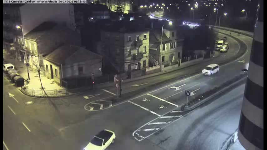 A nighttime, overhead view of a street intersection with several buildings and cars, under clear skies.