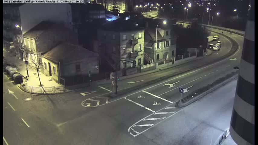 A nighttime, high-angle view of a road intersection with several buildings and a few vehicles on a curved roadway.