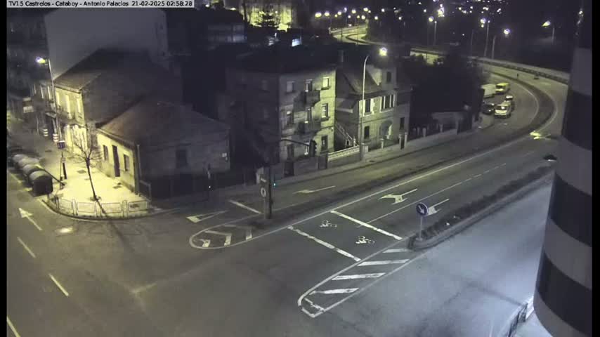 A nighttime street intersection showing several buildings and a few vehicles on the road under artificial light.