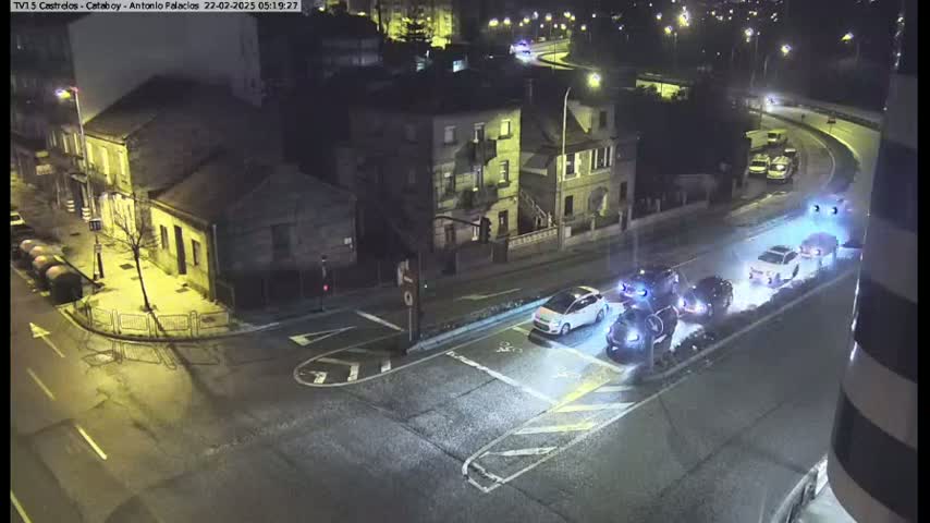 Several vehicles are stopped at a nighttime intersection near buildings under artificial light.
