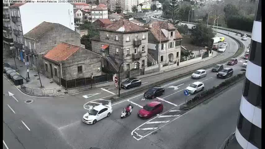 A street intersection with several cars and a scooter, viewed from above on an overcast day.