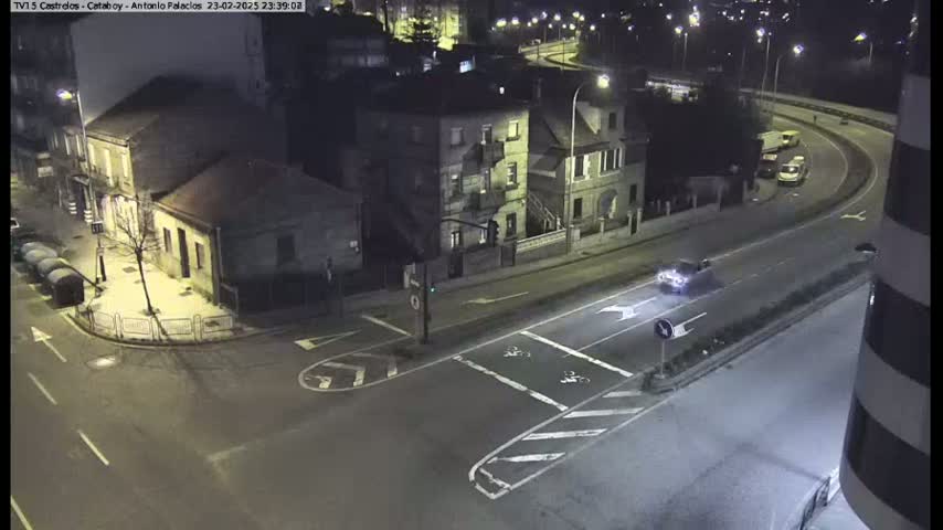 A high-angle nighttime view of a street intersection with several buildings and a few vehicles, under artificial light.