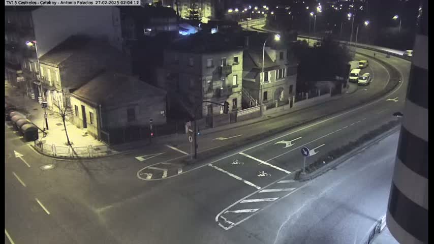 A nighttime, high-angle view of a street intersection and curved roadway with several buildings and a few vehicles.