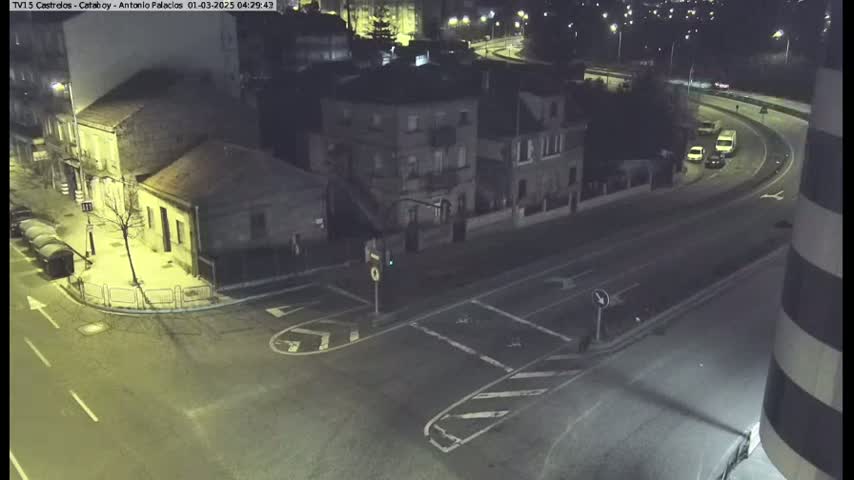 A nighttime aerial view of a street intersection with several buildings and a few vehicles on a nearby roadway.