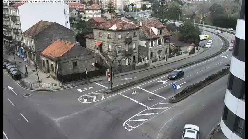 An overcast day reveals a street intersection with several cars and buildings, including a two-story house with a reddish-brown roof.
