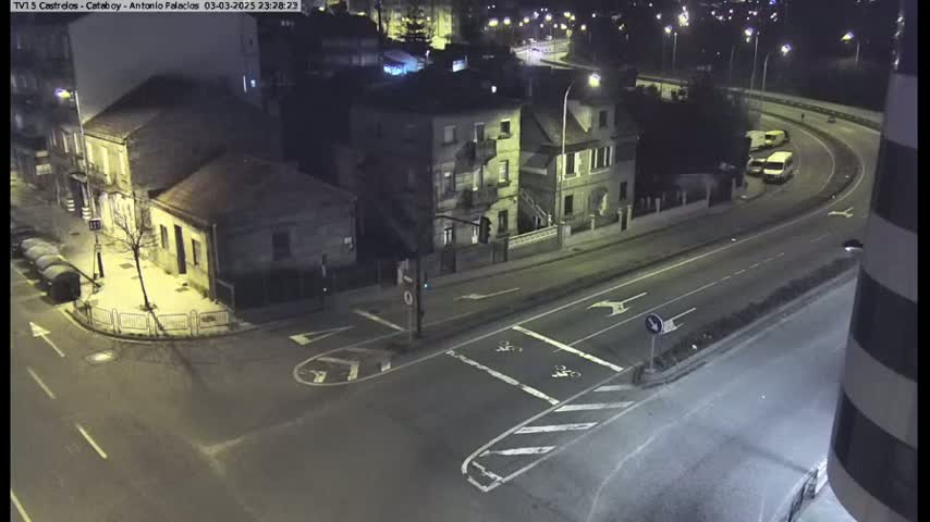 A nighttime aerial view shows a street intersection with several buildings and a few vehicles on a nearby highway.