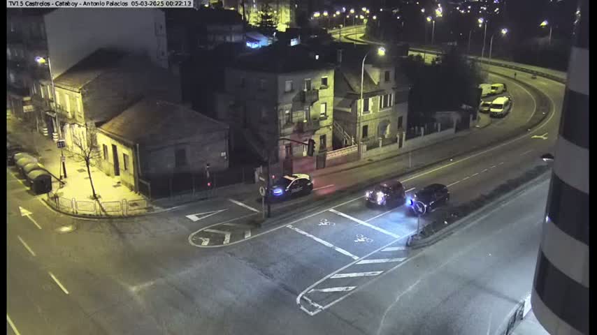 At night, several cars are stopped at a street intersection near buildings under streetlights.