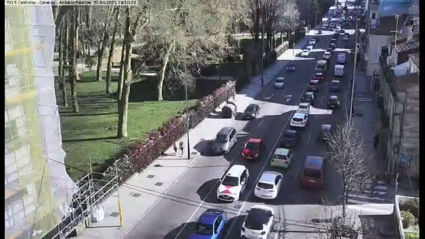 A sunny day shows a street with moderate traffic passing through a park-like area next to a building under construction.