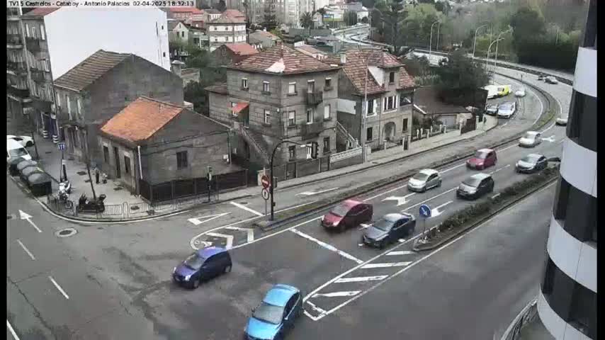 A high-angle view of a city intersection with several cars, and several buildings, on an overcast day.