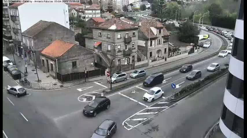 A street intersection with several cars, some buildings, and a road with moderate traffic on an overcast day.