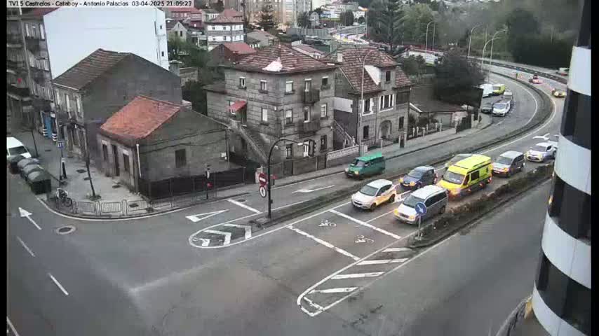 A street intersection in a city with several cars and buildings, on a cloudy day.