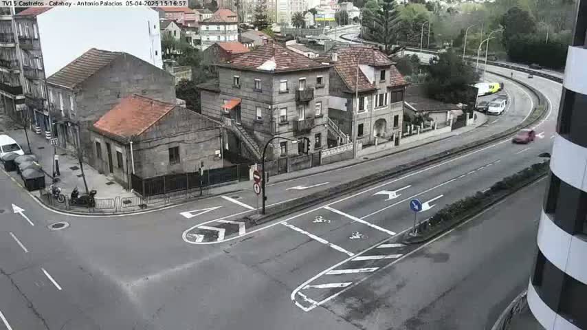 A high-angle view of a street intersection in an overcast urban setting, with several buildings and a few vehicles visible, including some parked cars and a couple of motorcycles.
