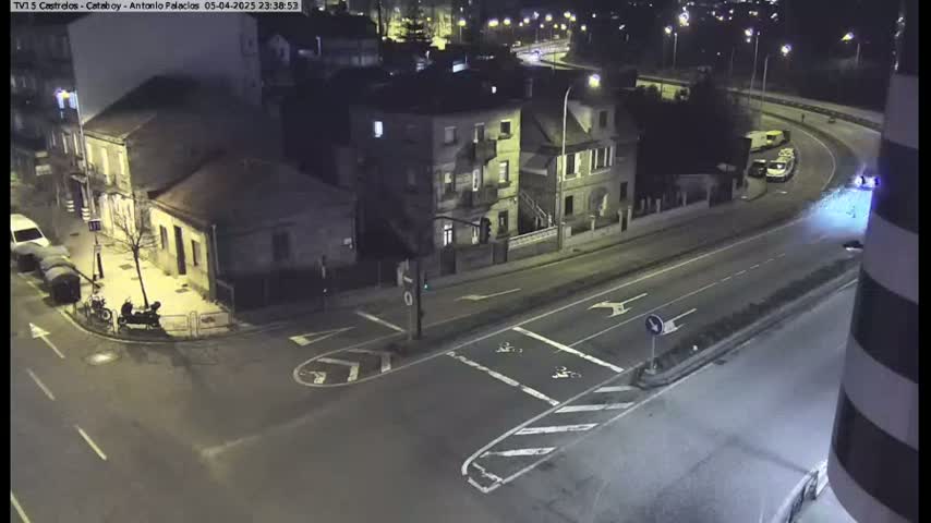A nighttime, high-angle view of a street intersection with several buildings and vehicles, including a few parked cars and a motorcycle.