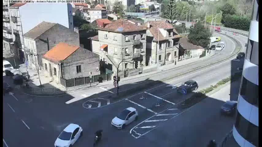 A sunny day shows a street intersection with several cars and buildings, including a multi-story building partially visible in the bottom right corner.