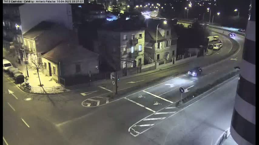 A nighttime, overhead view of a street intersection with several buildings and a few vehicles driving on the roads.