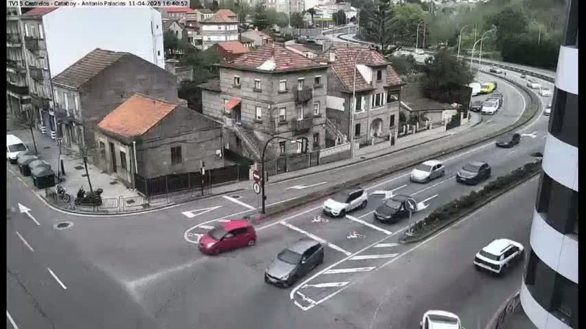 A street intersection with several cars and buildings, including a multi-story building, under overcast skies.