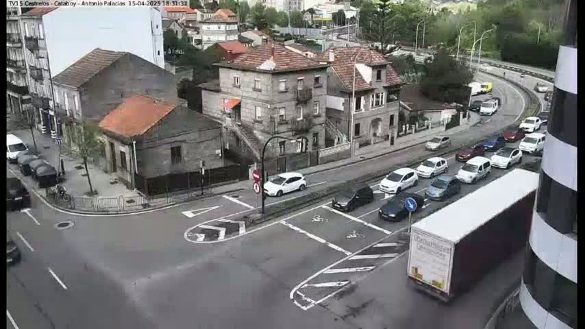 A street intersection in a town with several cars and buildings, under an overcast sky.