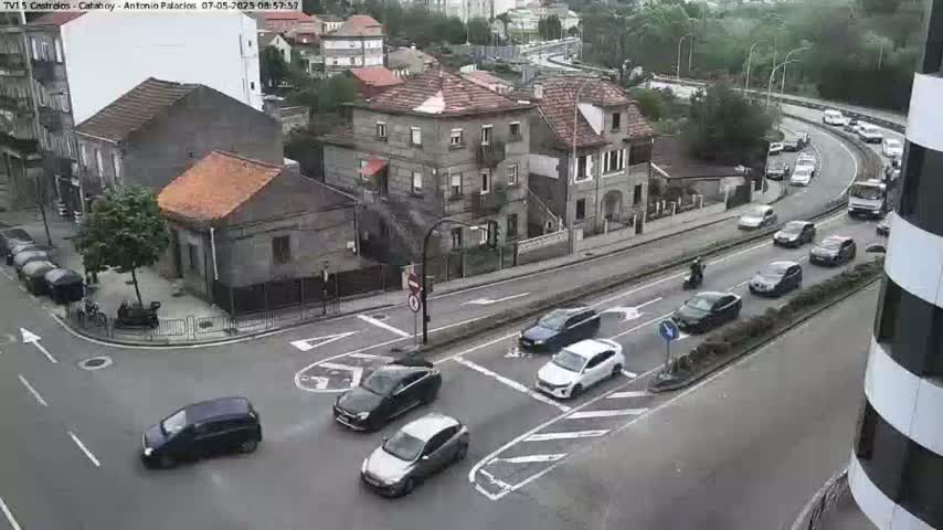 An overcast day reveals a street intersection in a town with several cars, buildings, and a few pedestrians.