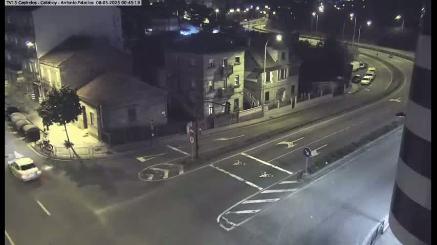 A nighttime aerial view shows a street intersection with buildings and a few cars, under dark and clear conditions.