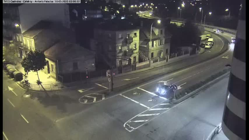 A nighttime, high-angle view of a street intersection with several buildings and a few cars, one of which is stopped at the intersection.