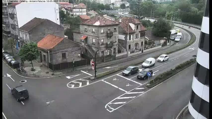 A street intersection with several cars and buildings, viewed from above on a cloudy day.