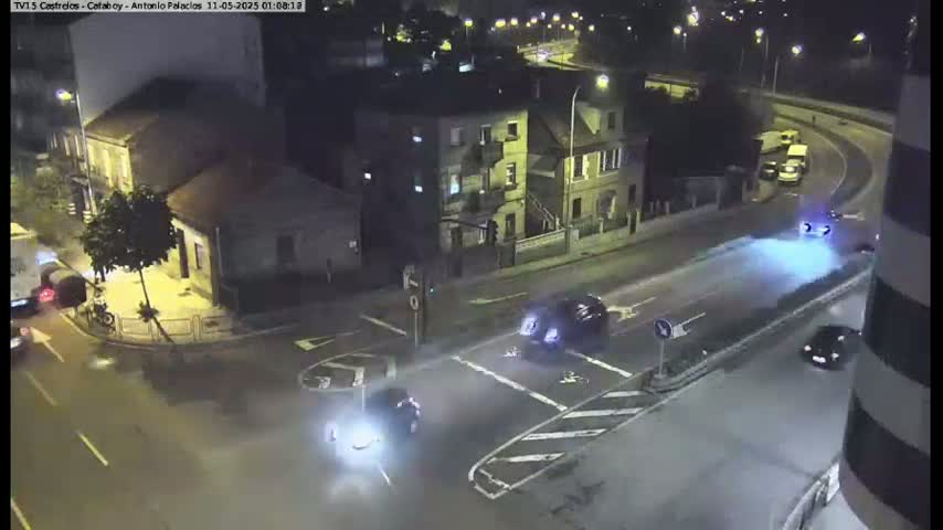 A nighttime, high-angle view shows several cars at an intersection in a city, with streetlights illuminating the scene.