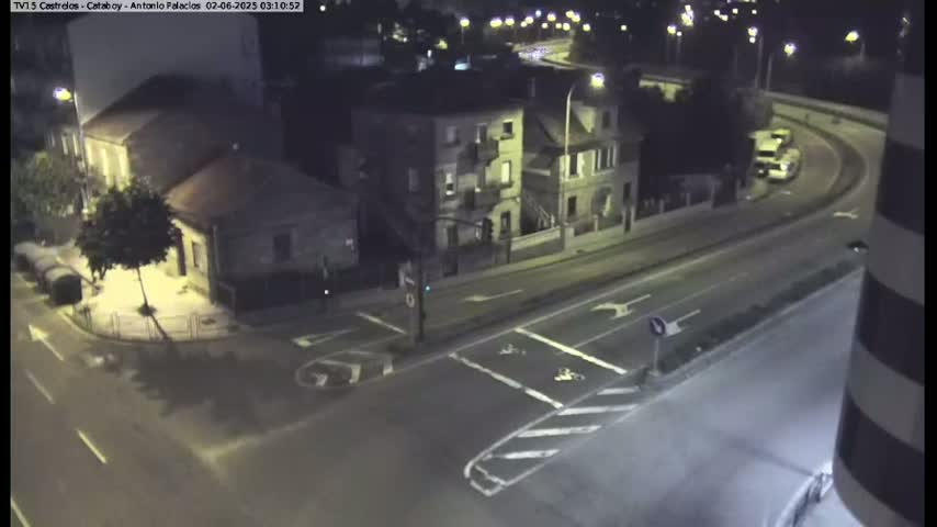 A nighttime, high-angle view shows a street intersection with two buildings and a curved road with minimal traffic.