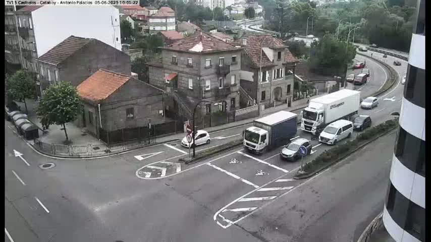 A street intersection with several cars and trucks, some of which are stopped, is seen on an overcast day near a collection of buildings.
